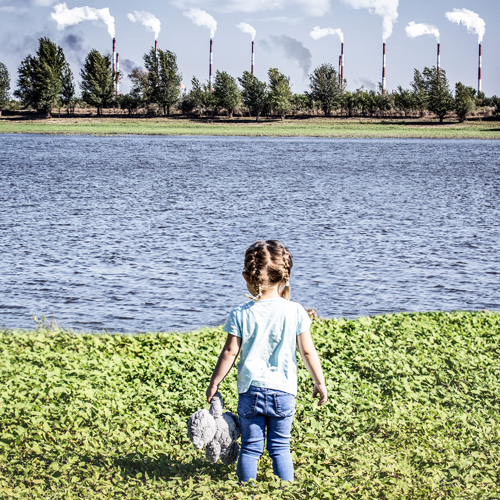 girl looking at pollution producing manufacturing plant.